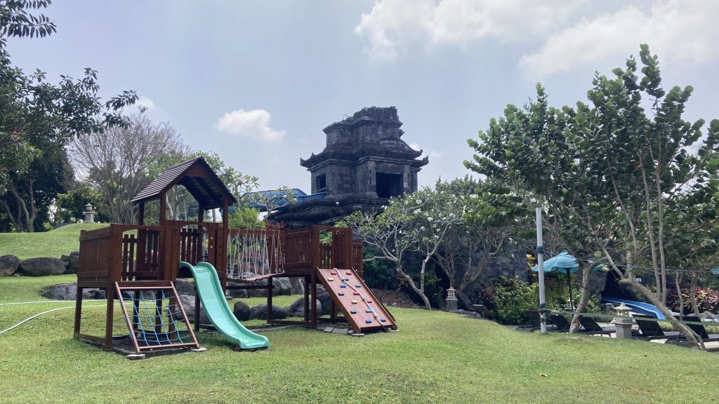 泳池旁草地上的兒童遊戲區，後方是仿寺廟的石造建築，也是滑水道入口