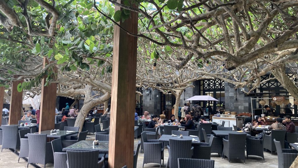早餐時段的室外用餐區，座位在大樹遮蔭下